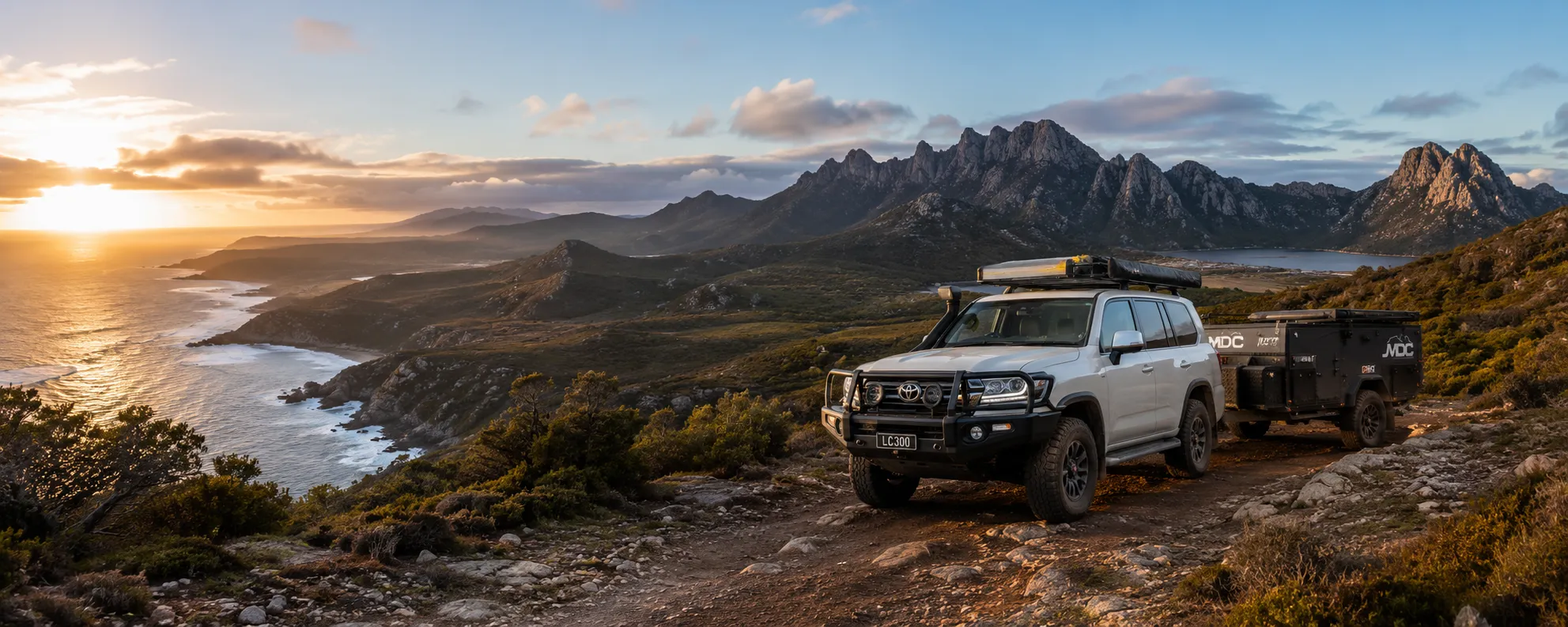 4WD and caravan parked above the Tasmanian coast at sunset with the Hazards mountain range beyond